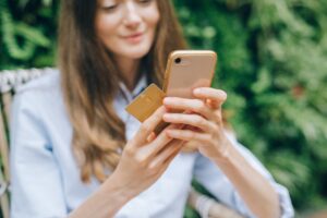 Woman outdoors holding a gold card near her phone, suggesting mobile payment or card use.